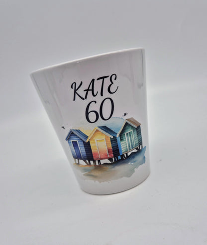 White plant pot with colourful beach huts design and 'KATE 60' text on a white background