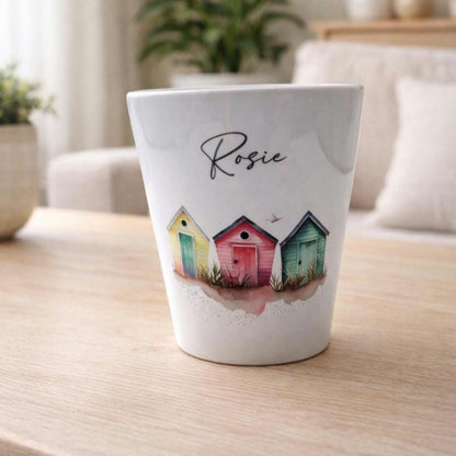 White plant pot with colourful beach huts design and 'Rosie' text on a wooden surface.